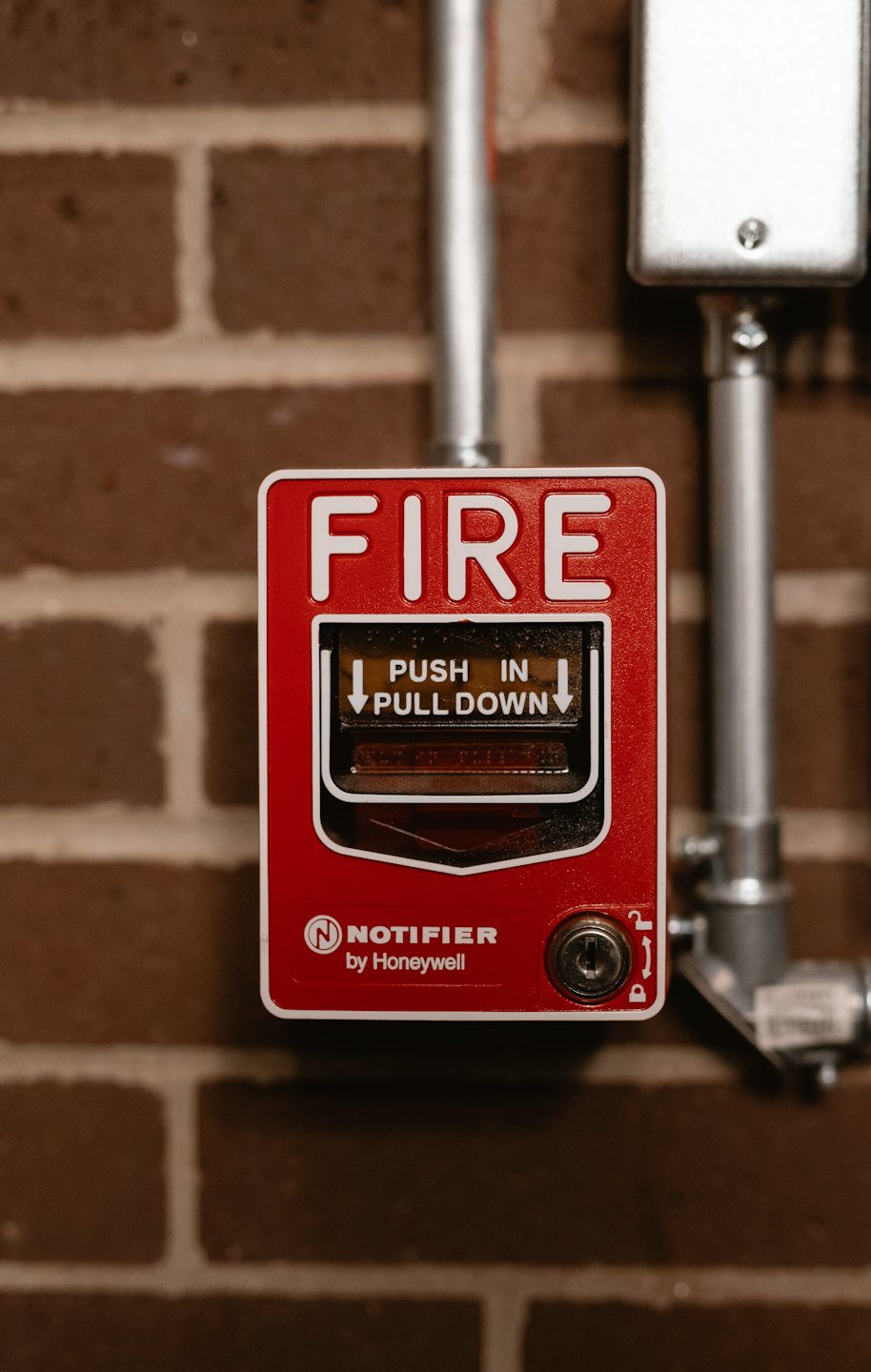 Red fire alarm pull station mounted on a brick wall.
